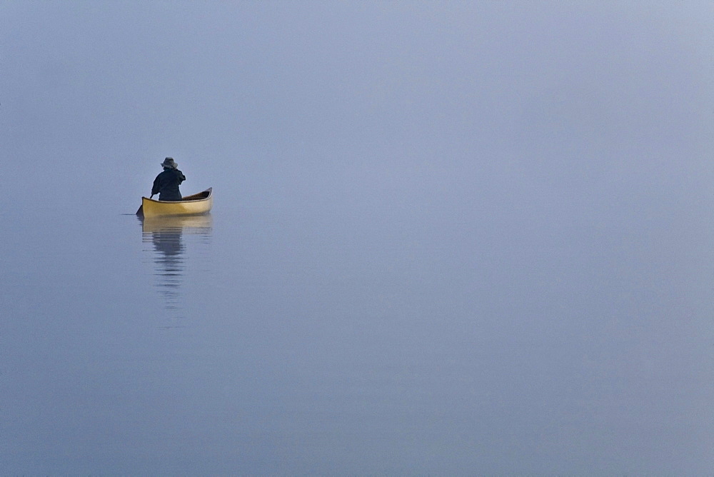 Woman paddling canoe in morning mist, Algonquin Park, Ontario