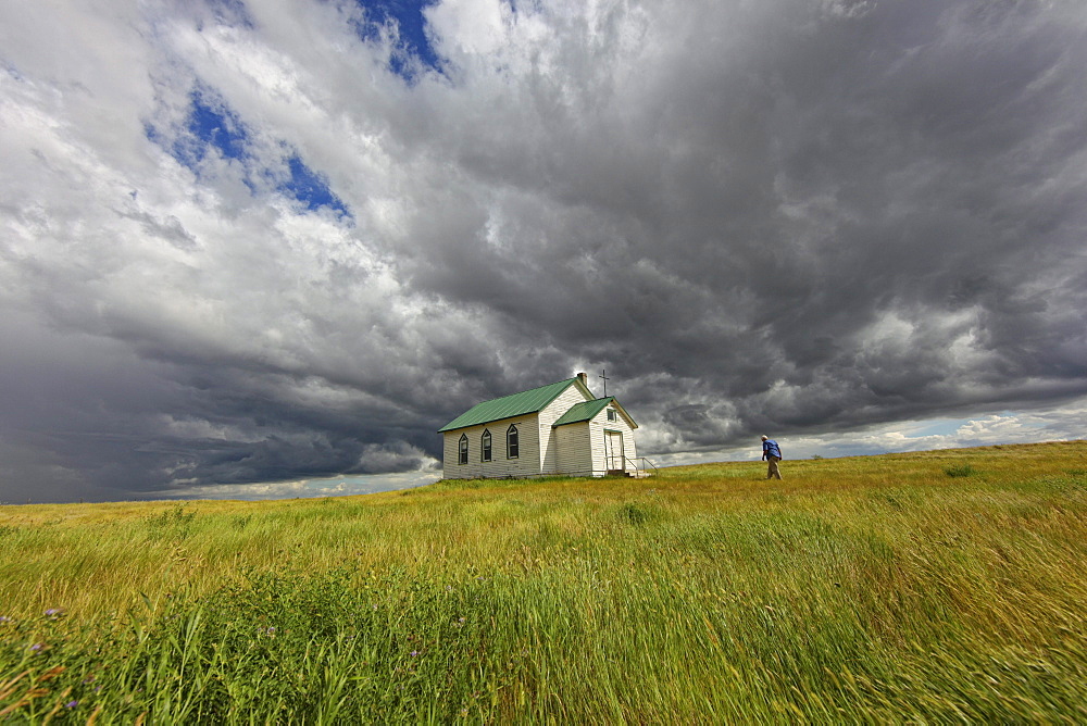 Man walking to abandoned church, with storm clouds overhead, Saskatchewan