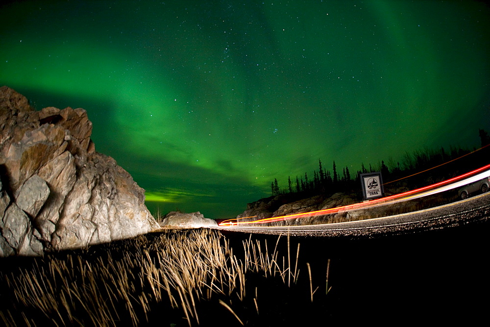 Lights of a passing vehicles under Aurora Borealis at the start of the Ingraham Trail, outside Yellowknife, Northwest Territories