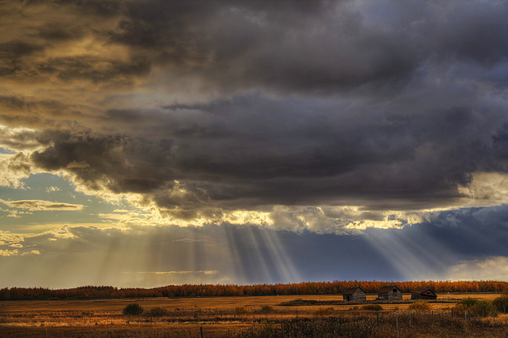 Sun Rays through Clouds over three Old Grain Bins, rural Alberta