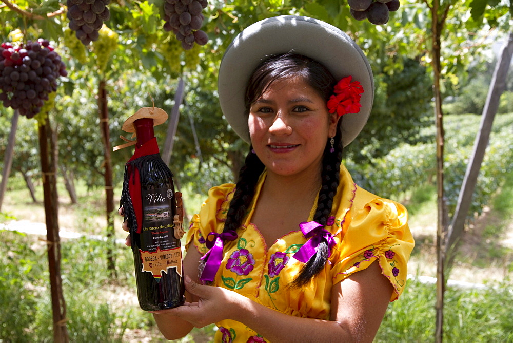 Chapaca holding a bottle of red wine in a vineyard of Calamuchita, Tarija, Bolivia