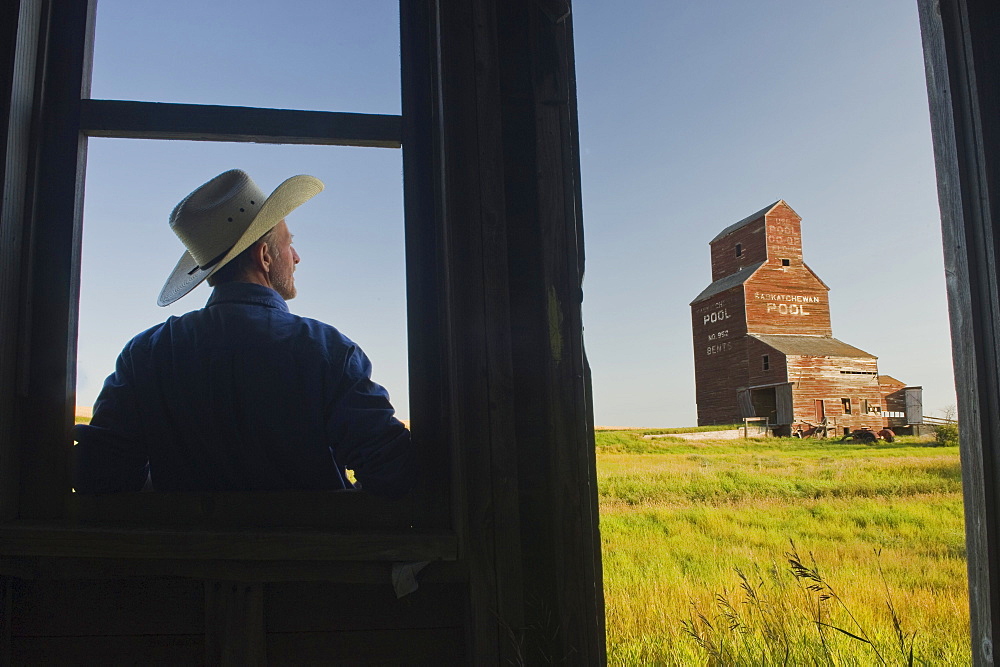 Farmer looking towards an abandoned grain elevator, in the ghost town of Bents, Saskatchewan