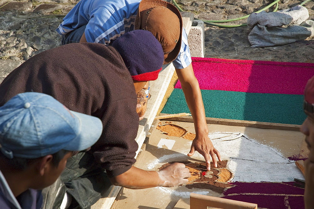 People making a carpet of sand & sawdust with the image of Jesus along the Good Friday processional route. Carpet-making is thought of as a sacrificial act, as the elaborate detail and time that go into the carpet making is a way for people to give something of themselves in memory of the crucifixion of Jesus. These carpets last on average 2 hours before they are destroyed by the many feet that march over them during a procession in Antigua Guatemala., Sacatepuquez, Guatemala