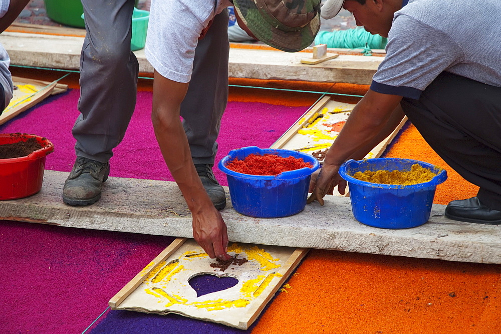 People working on a carpet made of sand & sawdust along the Good Friday processional route. Carpet-making is thought of as a sacrificial act, as the elaborate detail and time that go into the carpet making is a way for people to give something of themselves in memory of the crucifixion of Jesus. These carpets last on average 2 hours before they are destroyed by the many feet that march over them during a procession in Antigua Guatemala., Sacatepuquez, Guatemala