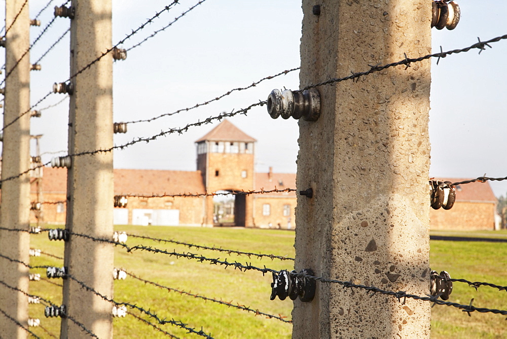 View of the Main Guard House through the electrified barbed wire fence separating sections of the Auschwitz-Birkenau Concentration Camp, Oswiecim, Malopolska, Poland