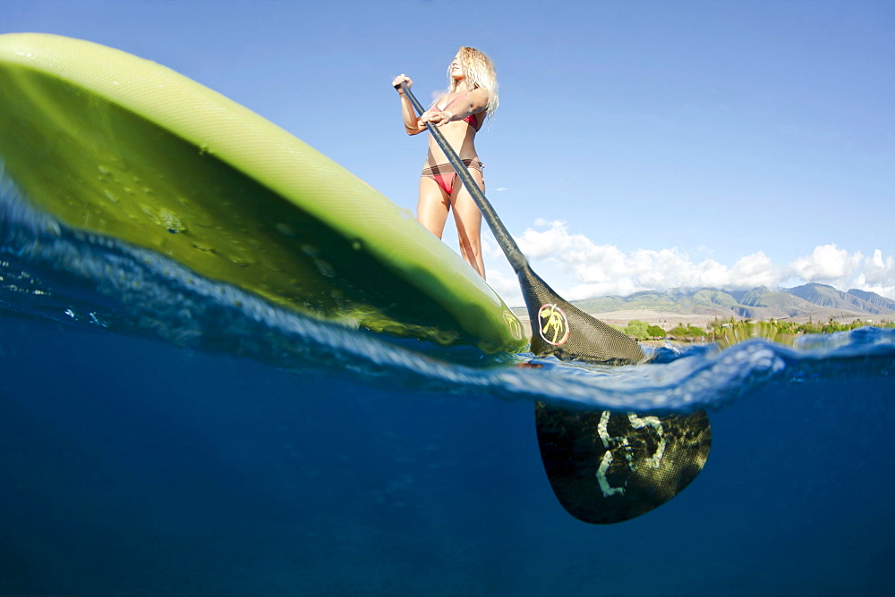 Hawaii, Maui, Woman stand up paddling in ocean just off Canoe Beach, Over/under view.