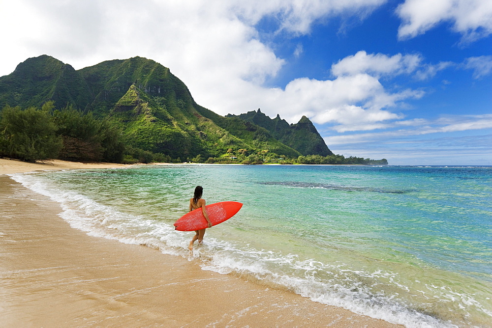 Hawaii, Kauai, Haena Beach Tunnels Beach, Woman entering ocean with surfboard.