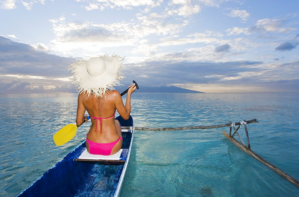 French Polynesia, Moorea, Woman paddling in ocean in outrigger canoe.