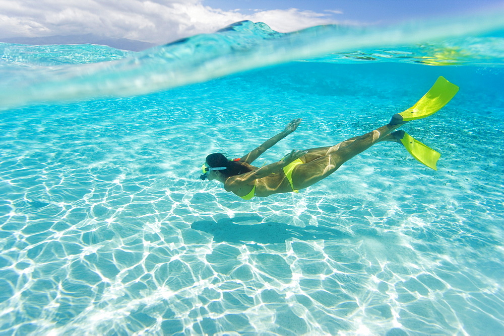 Woman snorkeling in tropical ocean water, Over/under view.