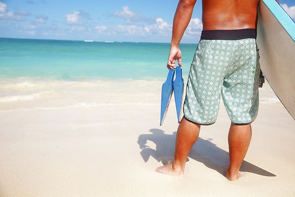 Hawaii, Oahu, Local Male holding a bodyboard and fins at the beach, view from behind.