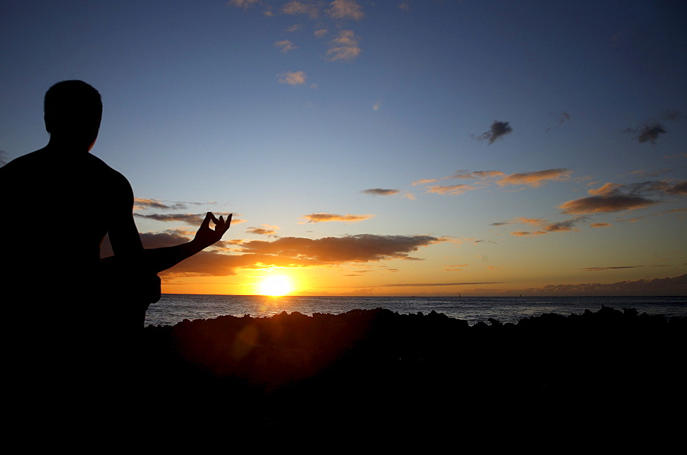 Hawaii, Oahu, Silhouette of a man meditating yoga as the sunsets