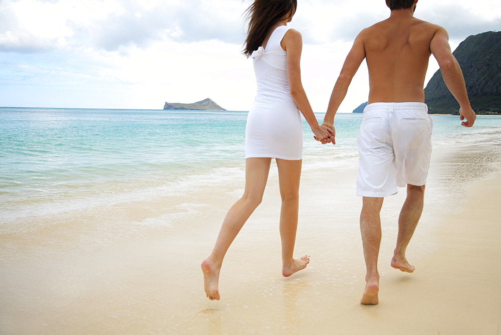 Hawaii, Oahu, Waimanalo, Young couple holding hands running together along the beach