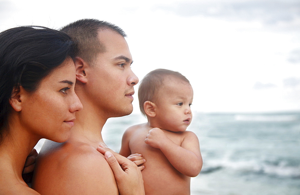 Hawaii, Oahu, Profile portrait of young attractive family of three looking out at the ocean.