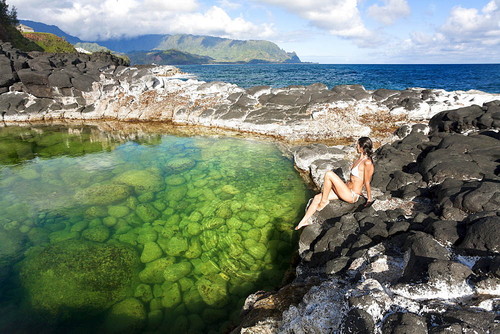 Hawaii, Kauai, Princeville, Queens Bath, Attractive woman sitting on rocks.