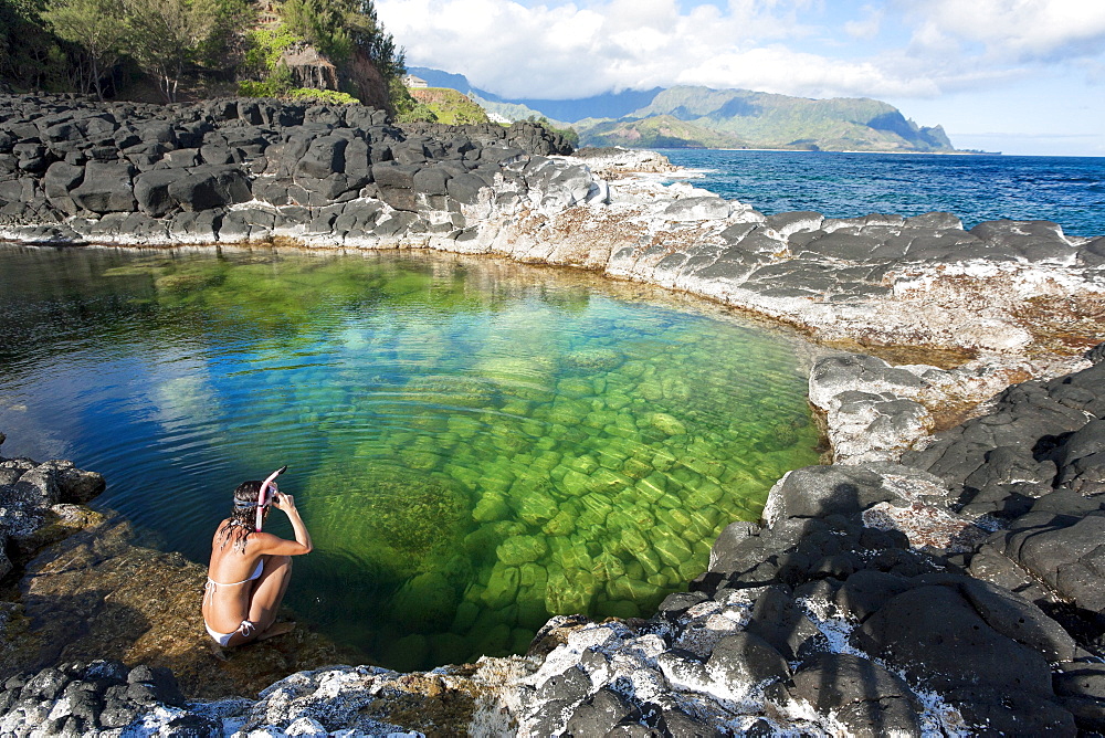 Hawaii, Kauai, Princeville, Queens Bath, Woman sitting on water's edge wearing snorkel gear.