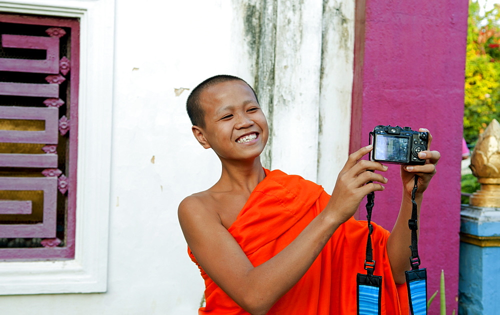 South East Asia, Laos, Luang Prabang, A young monk laughs as he takes his own picture with a visitor's camera.