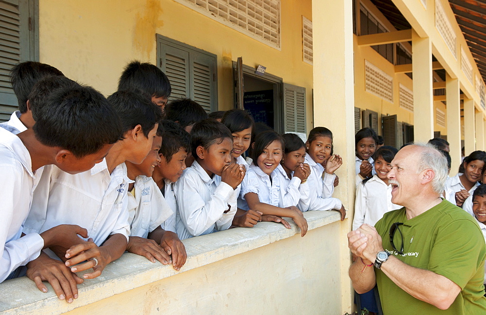 South East Asia, Cambodia, Siem Reap, A group of young school children laugh while tourist teaches them to make noises with their hands.