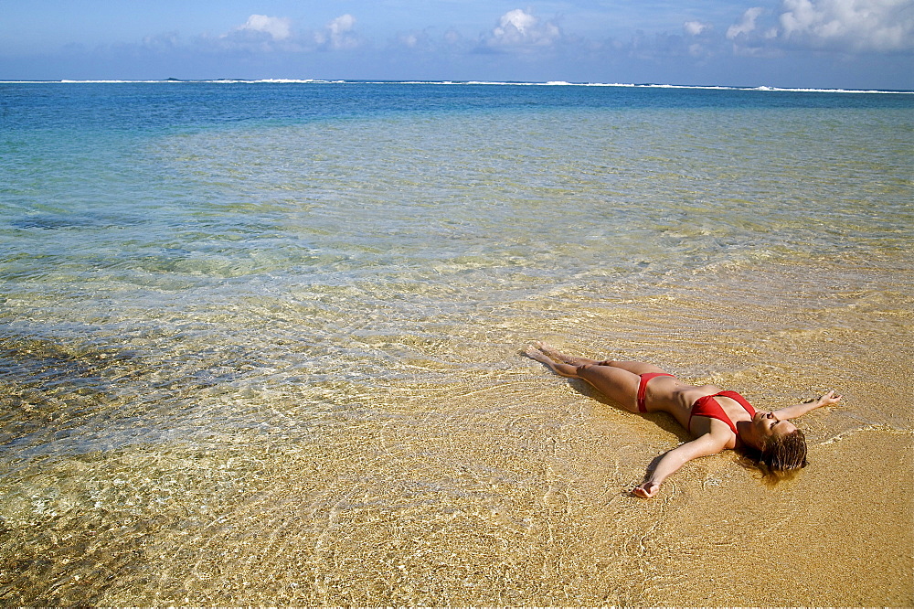 Hawaii, Kauai, Kealia beach, Woman laying on the beach in the shoreline.