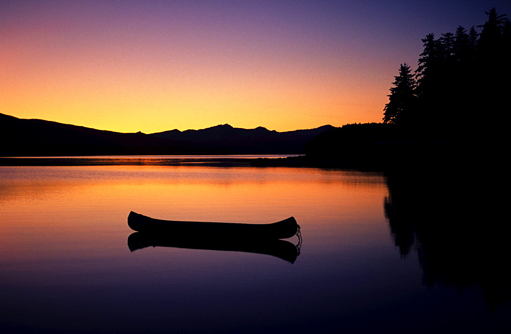 Alaska, Canoe floating on calm lake at sunset.