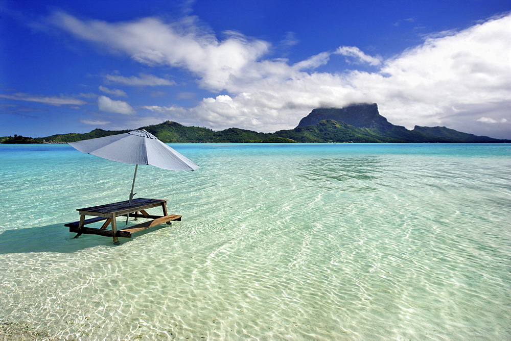 French Polynesia, Tahiti, Bora Bora, Picnic table and umbrella in clear lagoon water.