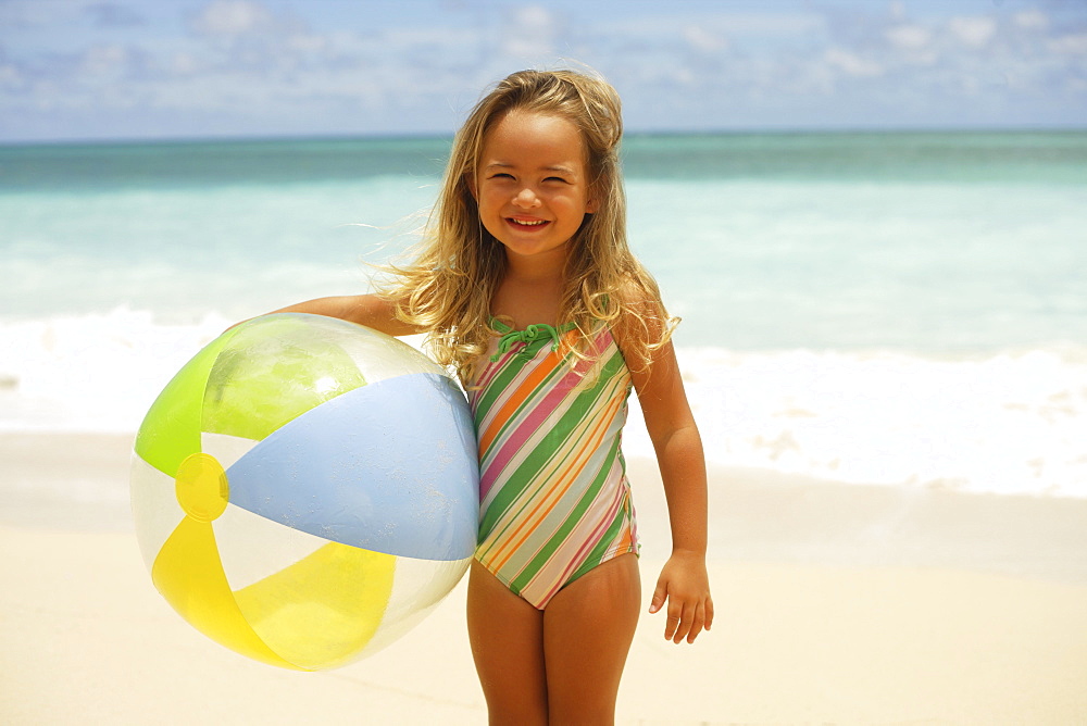 Hawaii, Oahu, little girl poses on beach with beach ball.