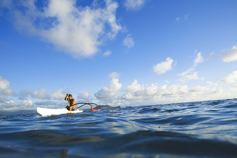 Hawaii, Oahu, Lanikai, man paddling one man outrigger canoe, land in background.