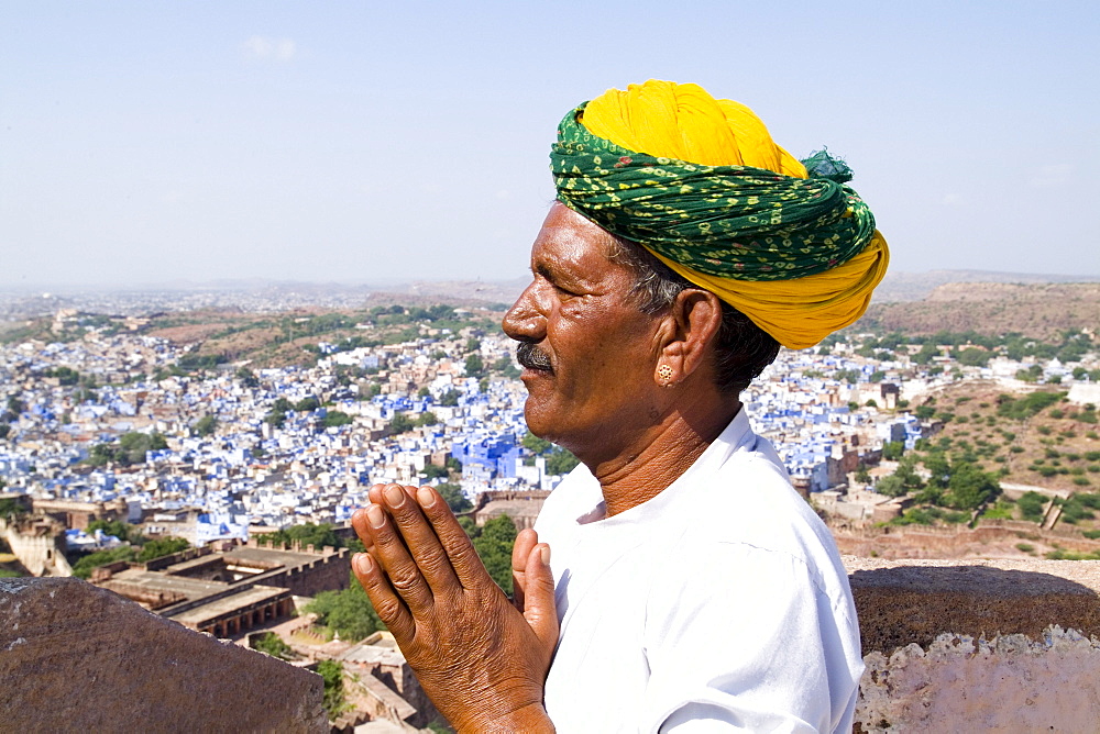 India, Rajasthan, Jodhpur, Hindu man praying at Fort Mehrangarh overlooking blue city.