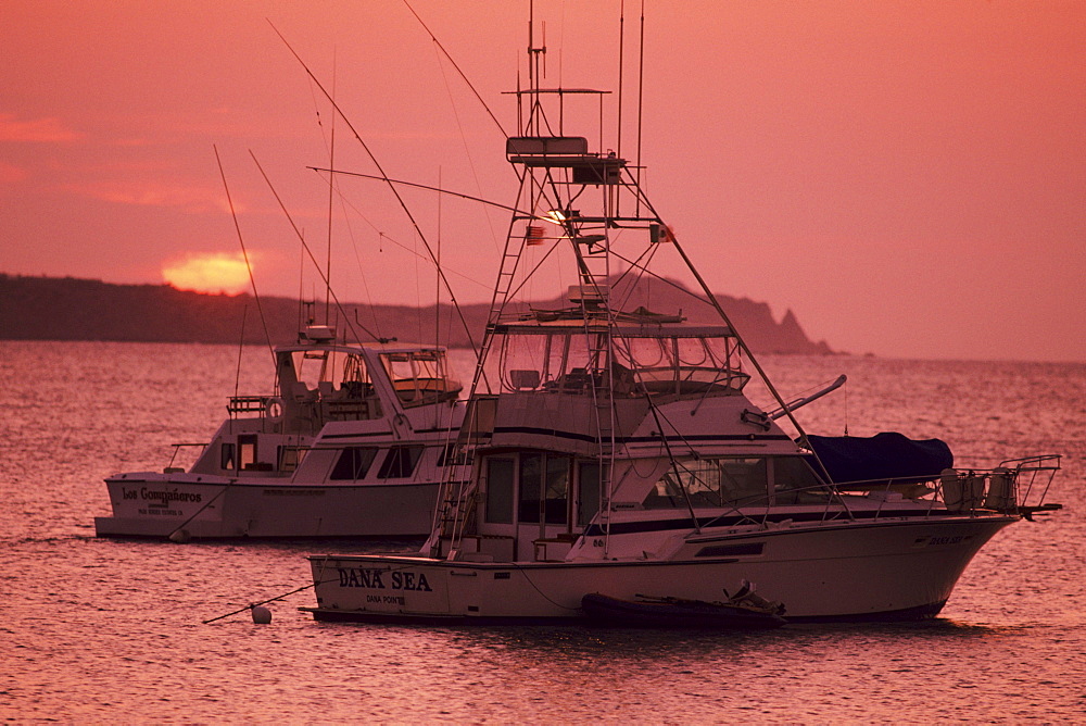 Mexico, Cabo San Lucas, Fishing boats floating on ocean at sunset.