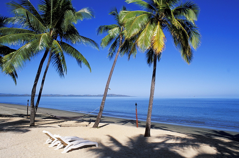 Fiji, Nadi Bay, Sheraton resort, white chairs on sandy beach, palm trees and shadows.