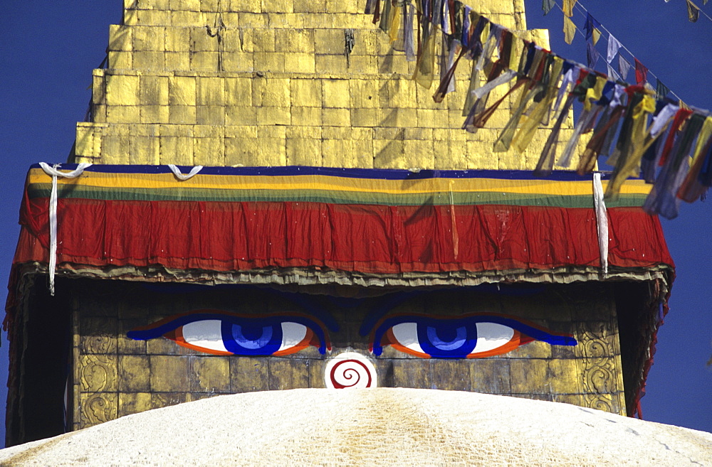 Nepal, Kathmandu, close-up of painted eyes on Boudhanath Stupa, colorful streaming flags.