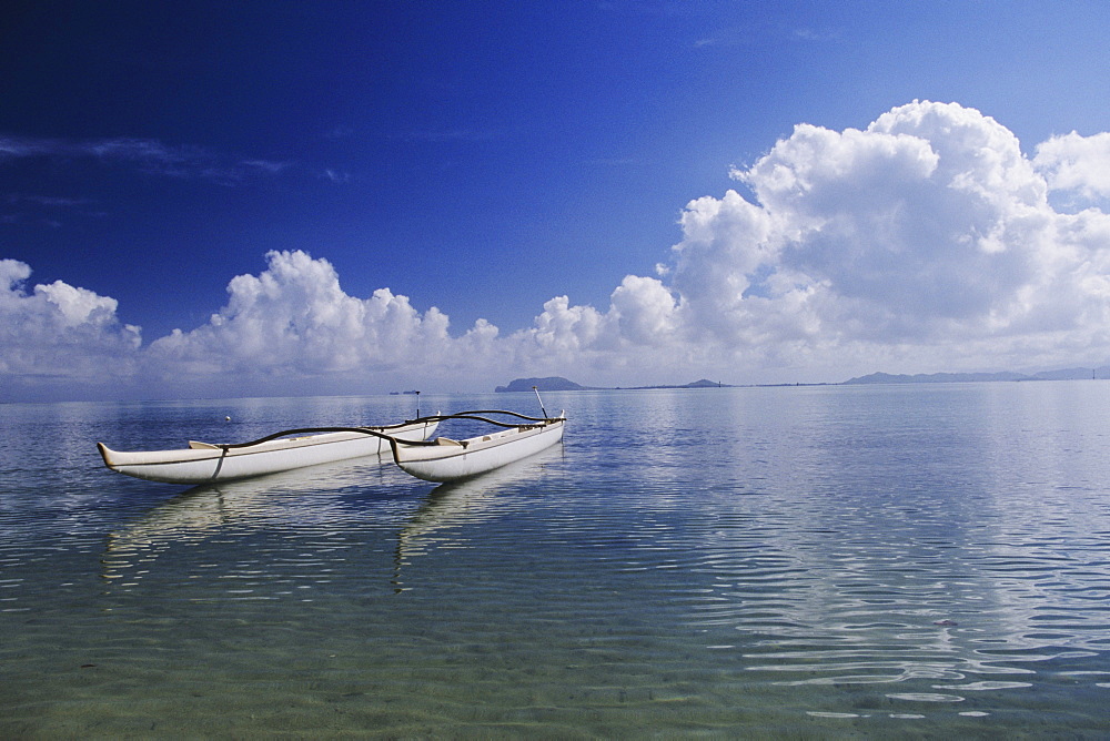 Hawaii, Oahu, Kaneohe Bay, Secret Island, White double hull canoe on calm ocean, blue sky.