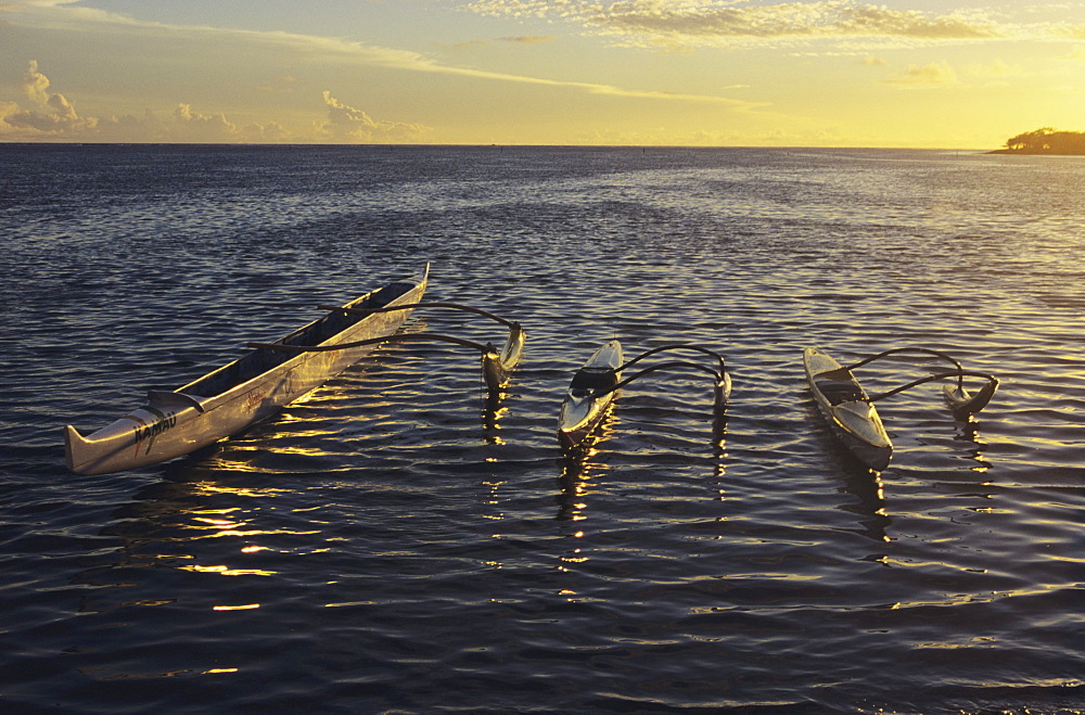 Hawaii, Three outrigger canoes float on rippling ocean water at sunset.