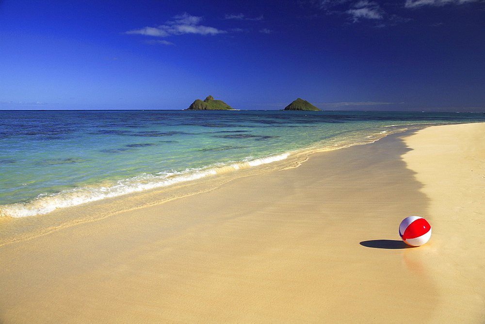 Hawaii, Oahu, Lanikai, Colorful beachball on the shore of tropical beach, Mokulua islands in background.