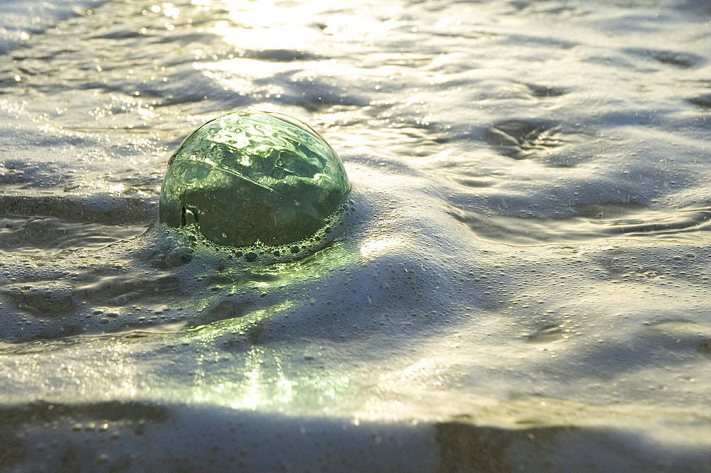 A glass fishing ball floats in shallow water, bright reflections