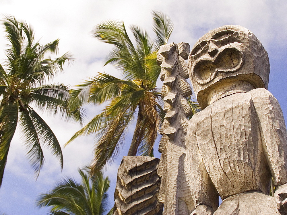 Hawaii, Big Island, Puuhonua O Honaunau, City of Refuge, Ki'i against blue sky and palm trees.