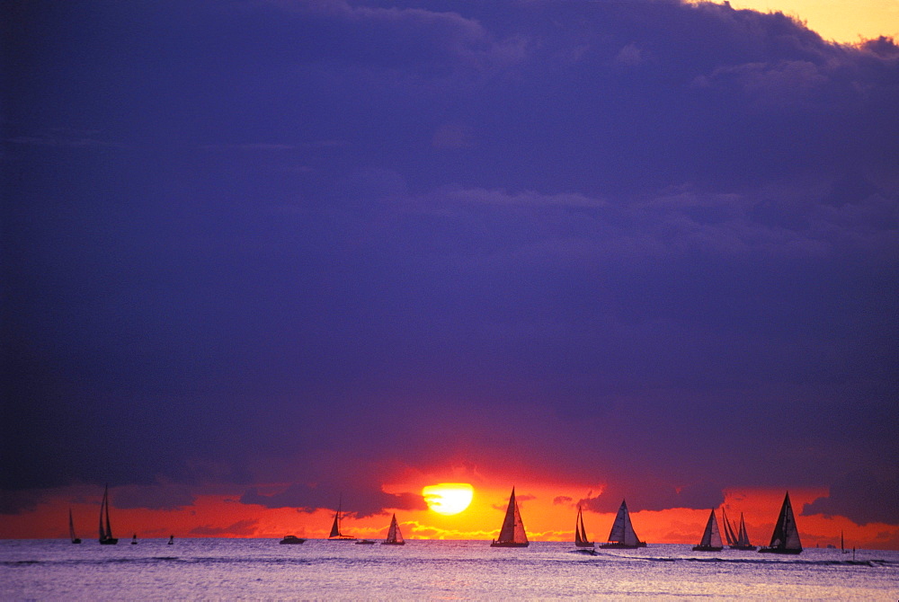 Hawaii, Oahu, Waikiki, Sailboats silhouetted on horizon at sunset