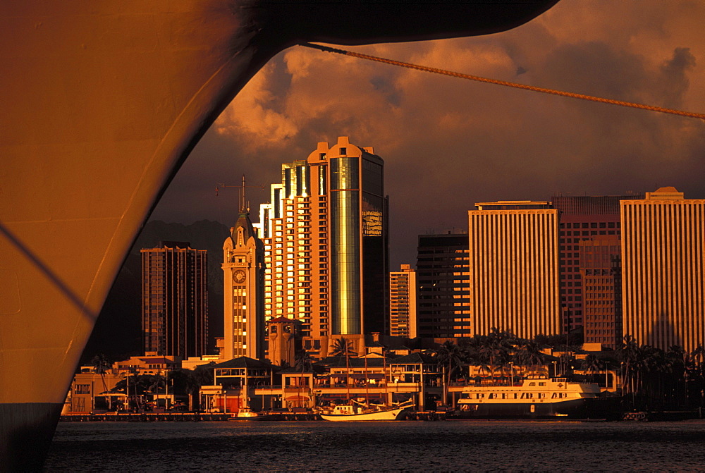 Hawaii, Oahu, Honolulu, Aloha Tower, Honolulu harbor, and downtown cast in a golden hue framed with ship