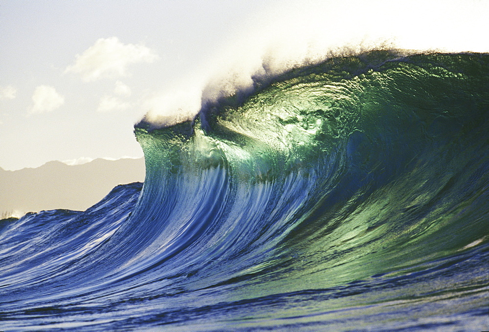 Hawaii, Oahu, North Shore; large green blue wave about to curl, mountains in background.