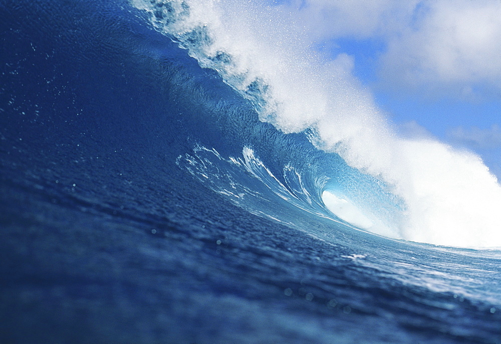 Hawaii, Curling wave, white spray, blue sky and clouds.