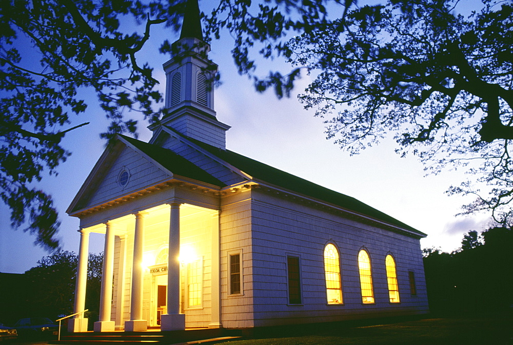 Hawaii, Kauai, Koloa Church exterior view illuminated at twilight, branches overhang purple sky