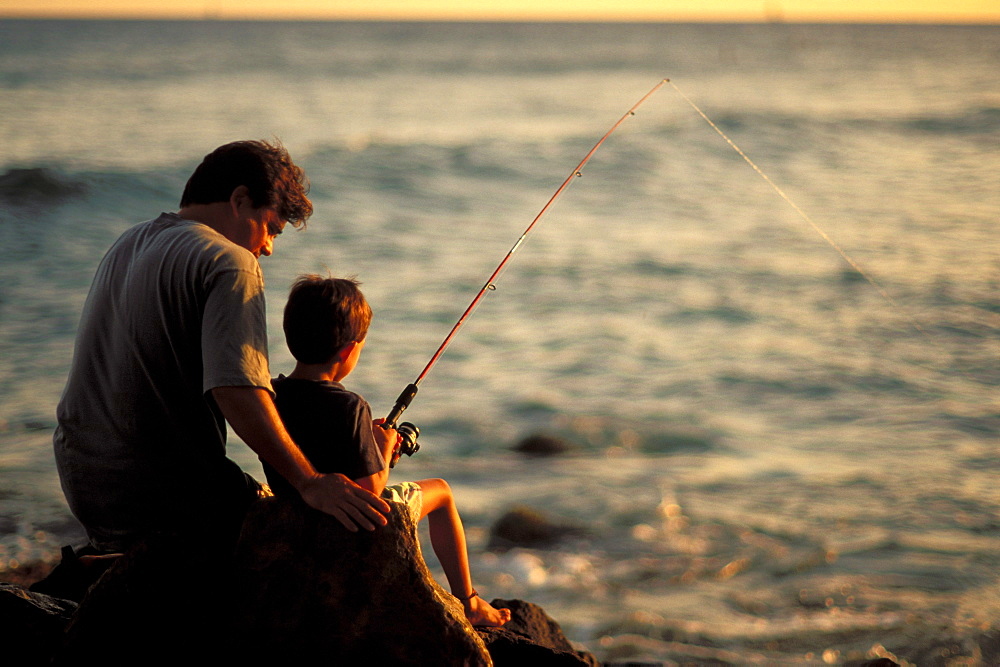 Local family, father and son fishing at sunset on rocks by ocean