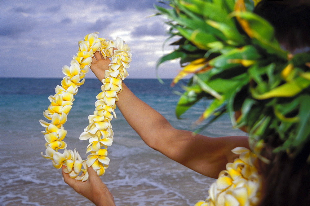 Woman hula along shoreline water, plumeria lei in arms outstretched, side view