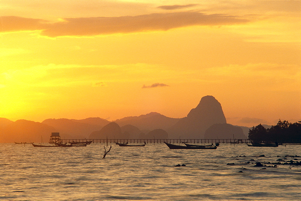 Thailand, Phangna Bay, boats anchored, pier and mountains at sunset golden orange sky