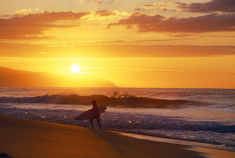 Hawaii, Oahu, North Shore, Silhouette of surfer walking out of ocean at golden sunset