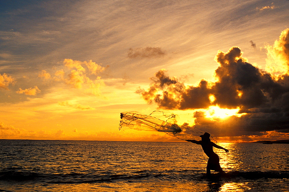 Fisherman throwing net at sunset