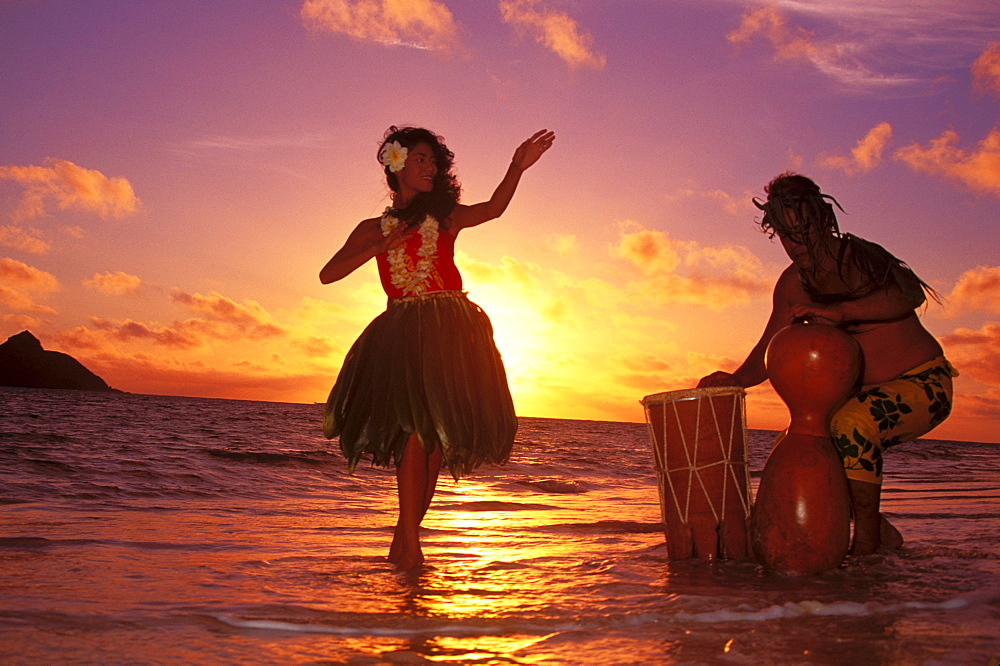 Hula dancer performing with drummer on beach at sunrise in background Hawaii