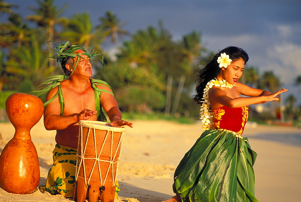 Hula dancer at sunrise on beach with Tahitian Drummer performing at water's edge