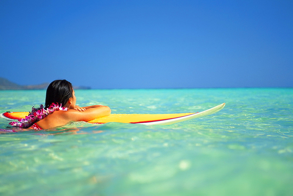 Hawaii, Oahu, Lanikai, Woman resting on surfboard looking out on clear teal water.