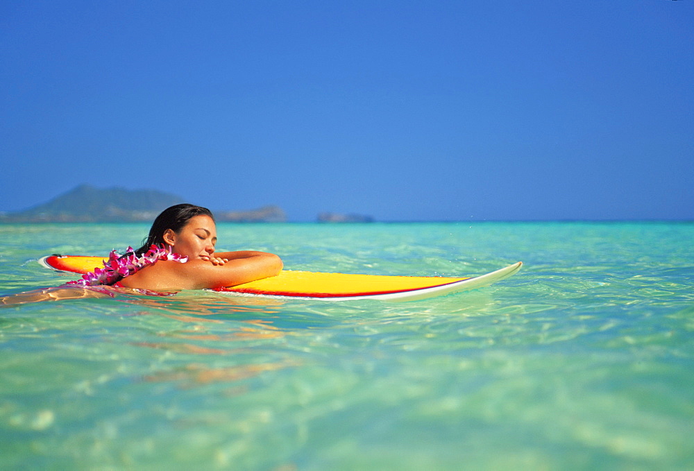 Hawaii, Oahu, Lanikai, Woman resting face of surfboard while in ocean with eyes closed