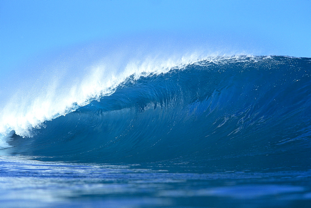 View of long, large, blue wave, curled at one end, blue sky in background 